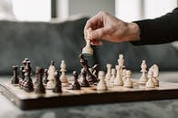 Artistic close-up of a hand moving a chess piece on a chessboard in a cozy setting.